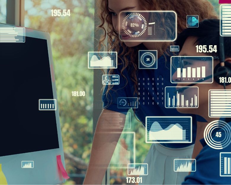 Two women analyze a computer screen displaying data icons related to calculating lifetime value.
